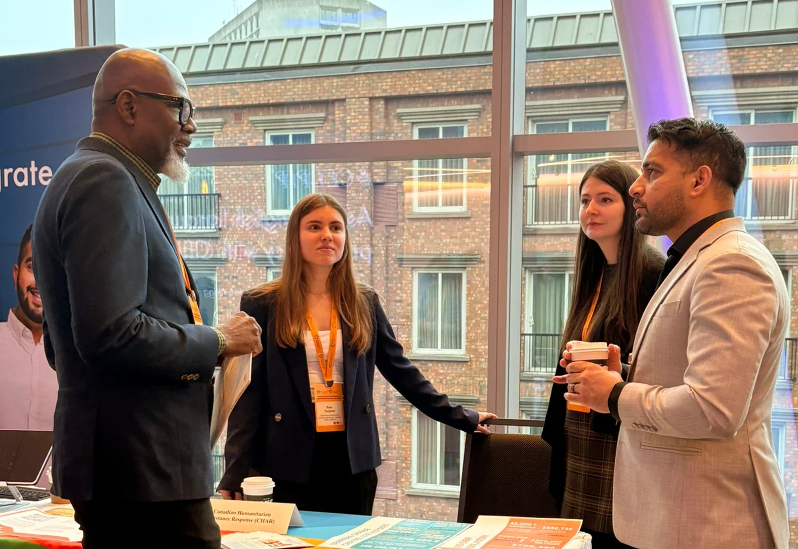 Four conference attendees in business dress talking beside an exhibitor booth.