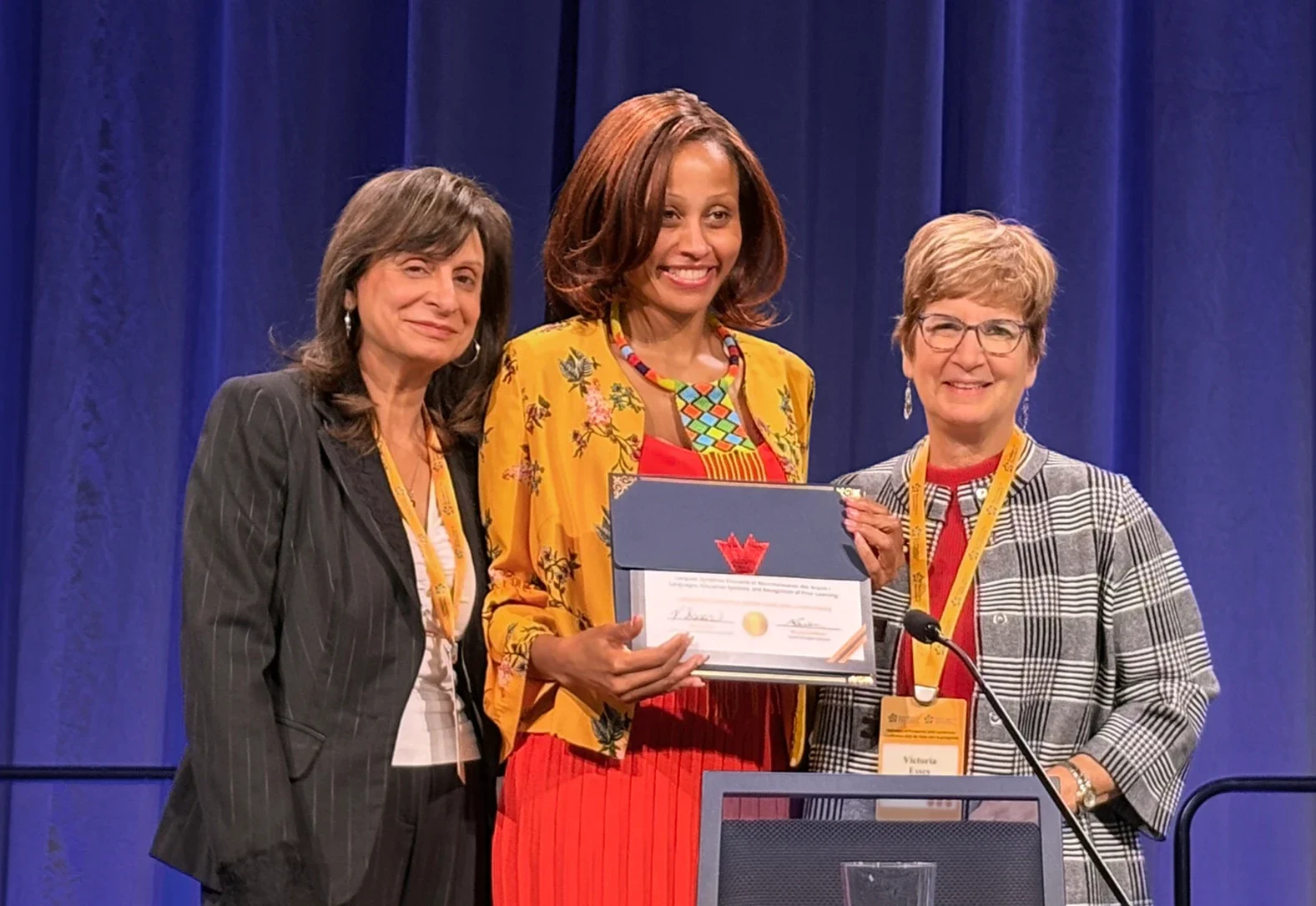 Three women on stage holding a framed award certificate at the P2P conference.