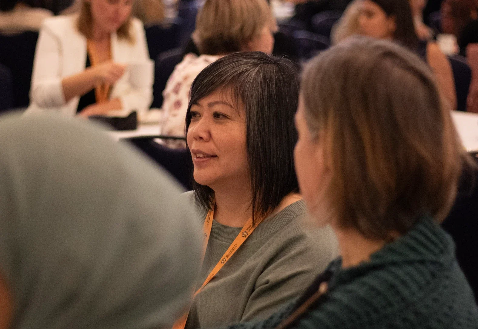 A conference attendee smiling in conversation at a crowded session table.
