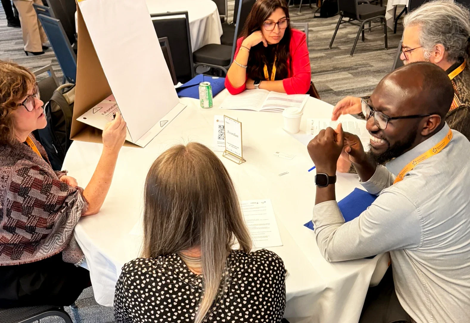 Five conference participants working around a round table with a flip chart and handouts.